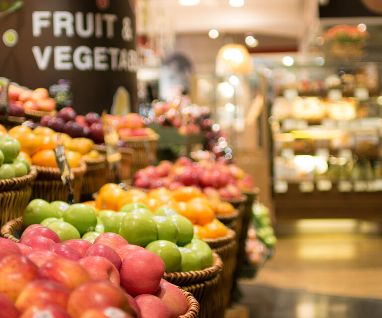 Es sind viele Körbe mit Äpfel in verschiedenen Farben im Supermarkt zu sehen.