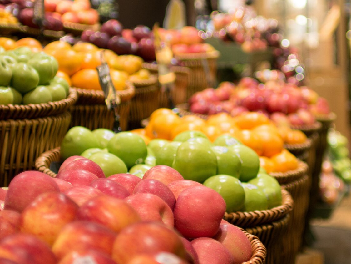 Es sind viele Körbe mit Äpfel in verschiedenen Farben im Supermarkt zu sehen.
