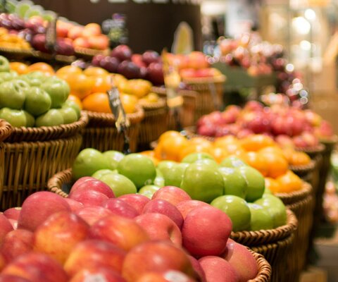 Es sind viele Körbe mit Äpfel in verschiedenen Farben im Supermarkt zu sehen.