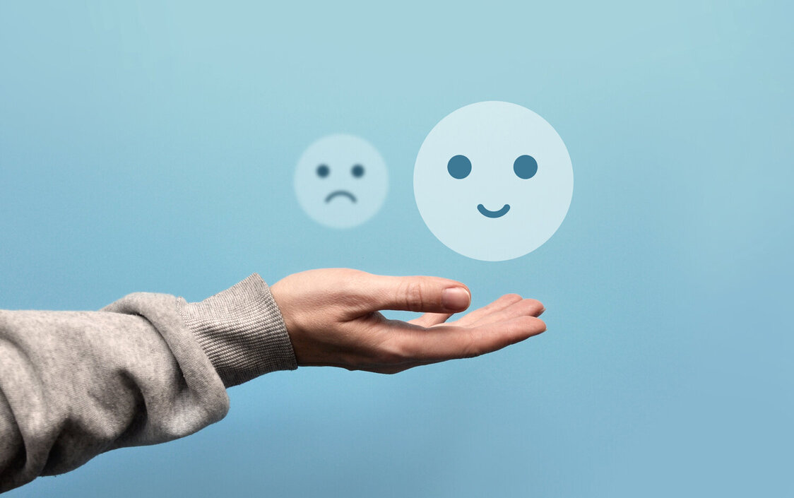 Über einer ausgestreckten Hand schweben ein fröhlicher und ein trauriger Smiley