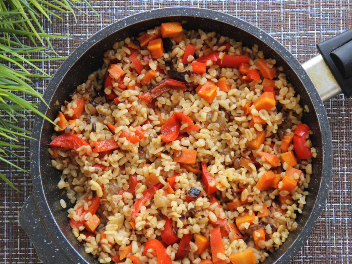  Eine Pfanne mit Bulgur und Paprikastücken. Daneben Schnittlauch.