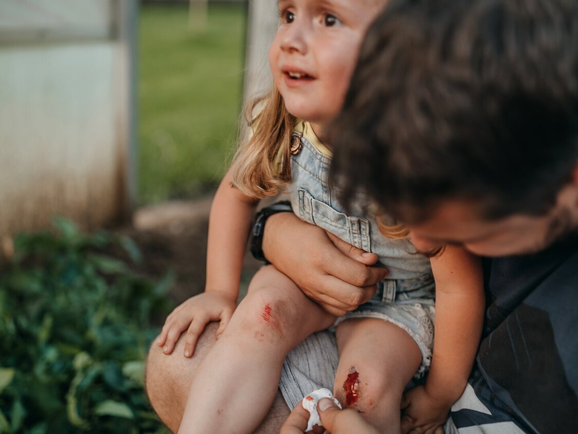 Kleines Mädchen mit einer blutenden Knieverletzug wird vom Vater versorgt.