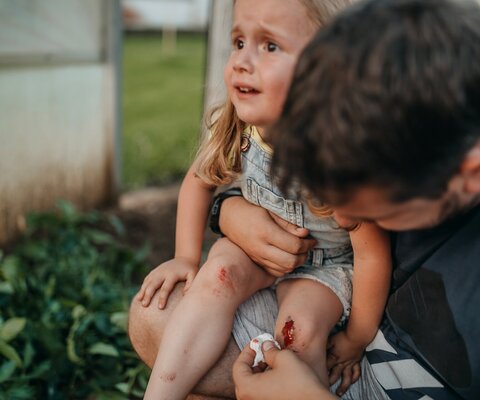 Kleines Mädchen mit einer blutenden Knieverletzug wird vom Vater versorgt.