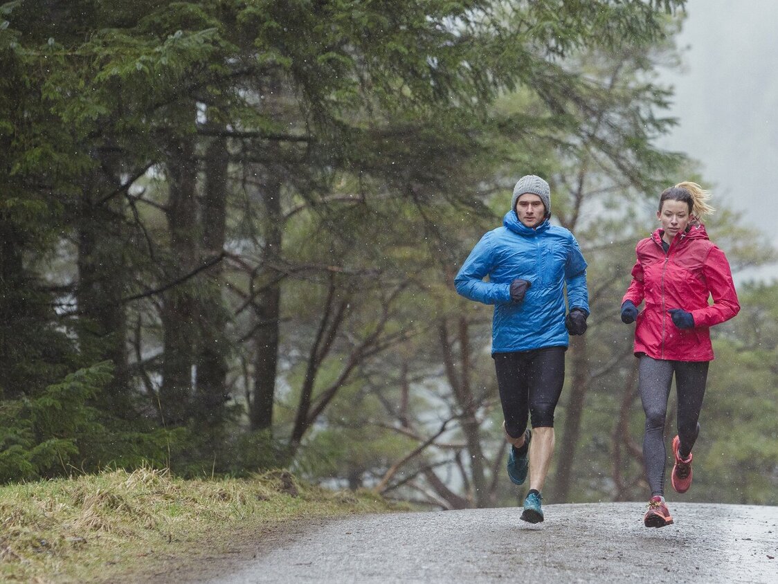 Ein Mann und eine Frau joggen bei Regen einen Waldweg entlang.