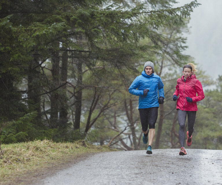 Ein Mann und eine Frau joggen bei Regen einen Waldweg entlang.