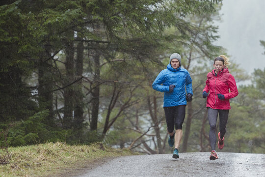 Ein Paar joggt bei schlechtem Wetter einen Waldweg entlang.