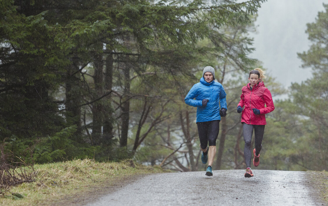 Ein Mann und eine Frau joggen bei Regen einen Waldweg entlang.