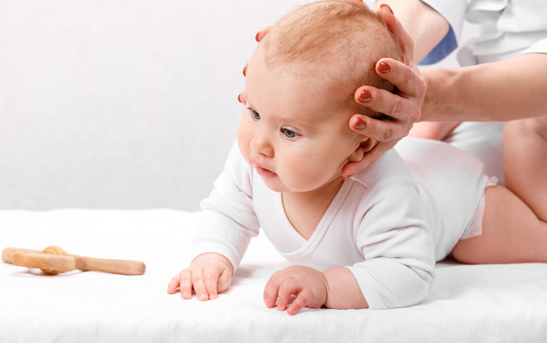 Ein Baby krabbelt, während eine Person seinen Kopf stützt.