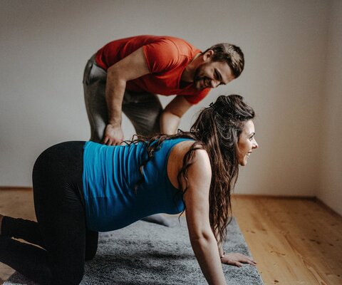 Eine schwangere Frau im Vierfüßler-Stand und ein Mann, der daneben steht.