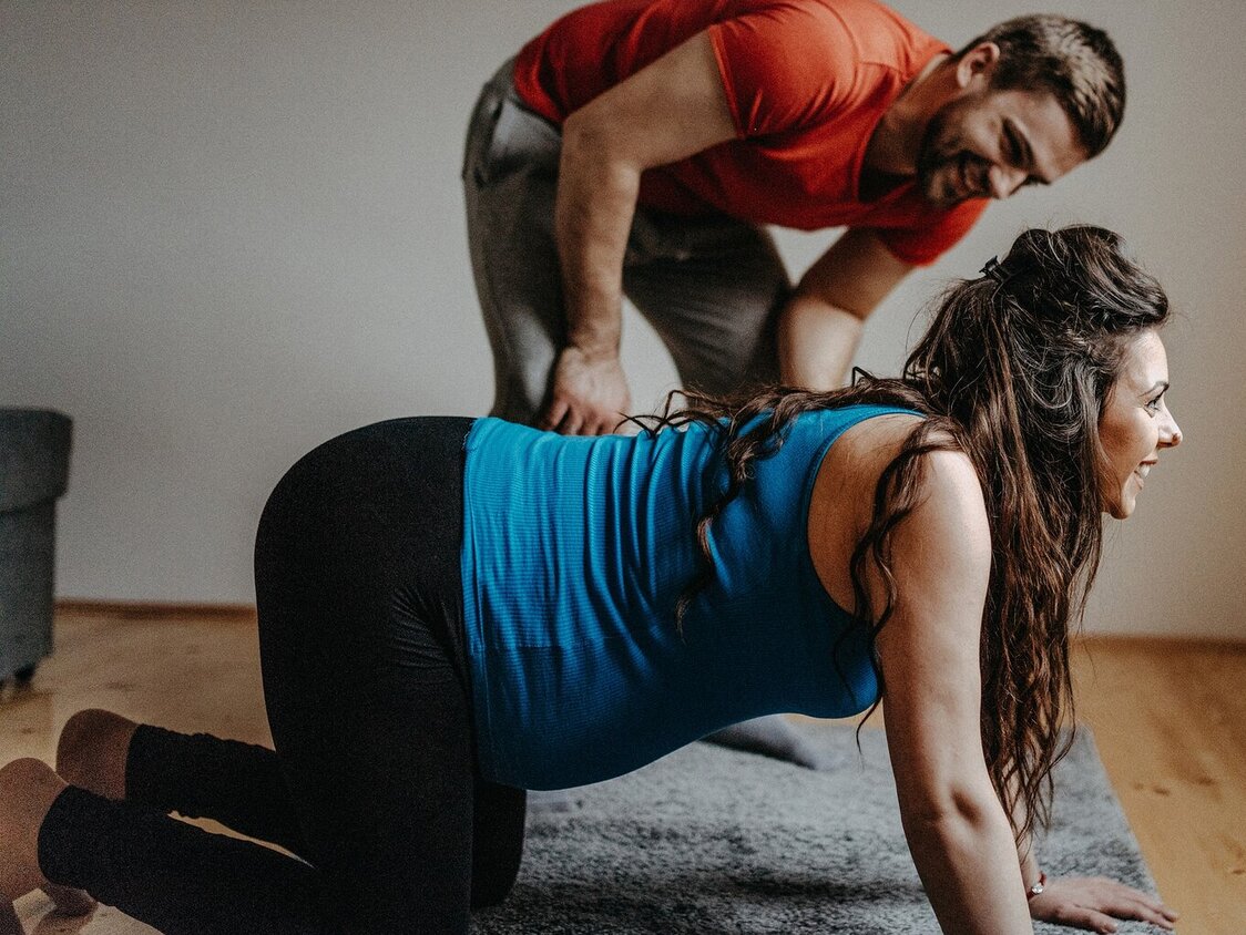 Eine schwangere Frau im Vierfüßler-Stand und ein Mann, der daneben steht.