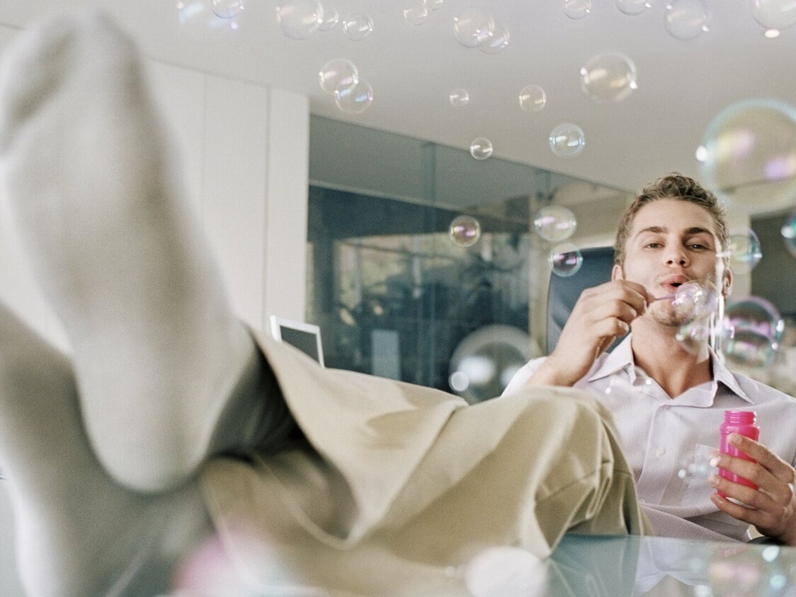 Ein Mann sitzt im Büro mit den Füßen auf dem Tisch und macht Seifenblasen.
