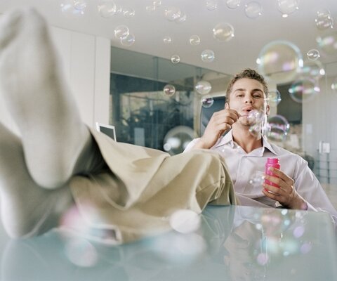 Ein Mann sitzt im Büro mit den Füßen auf dem Tisch und macht Seifenblasen.