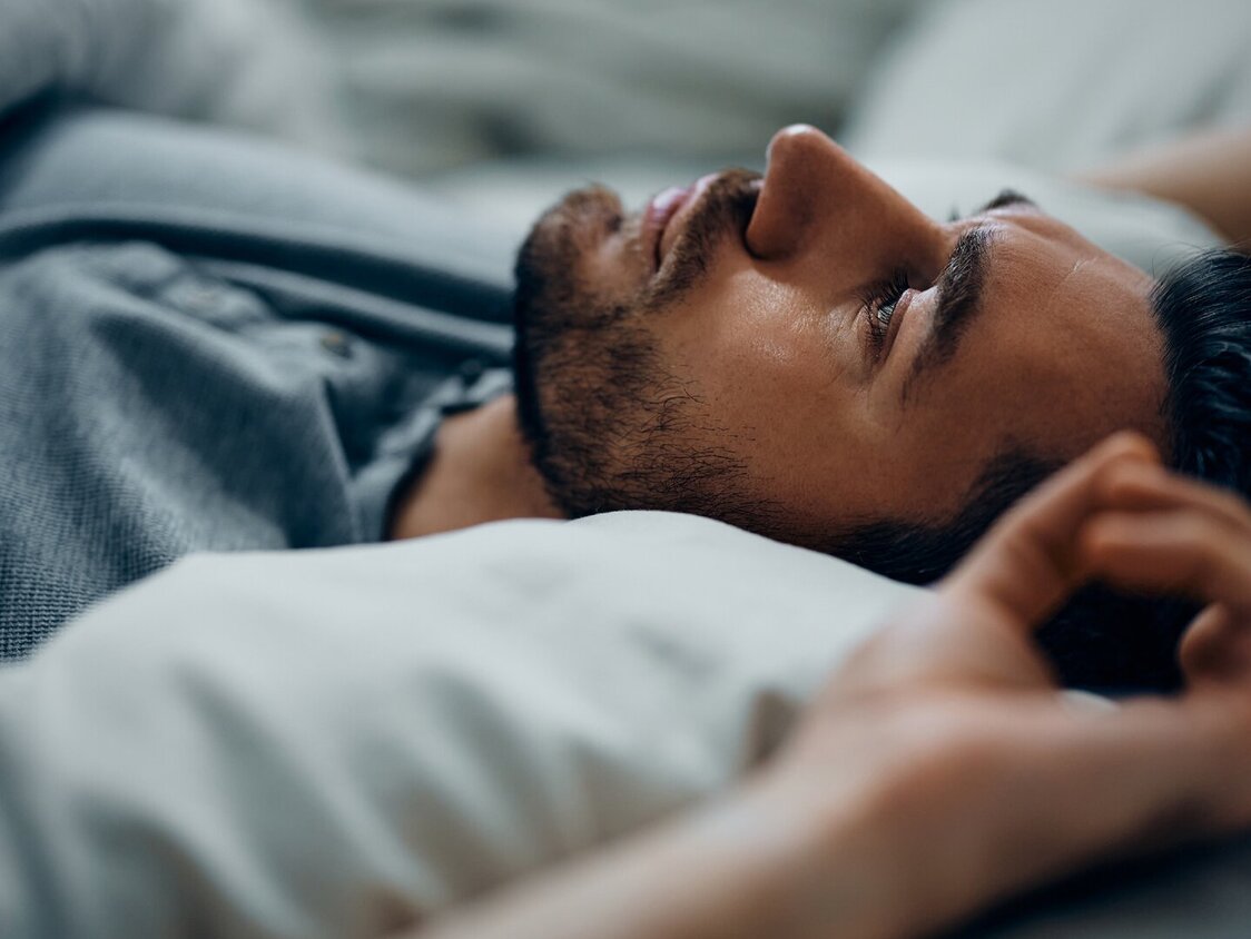 Ein Mann liegt auf dem Rücken im Bett und blickt nach oben.