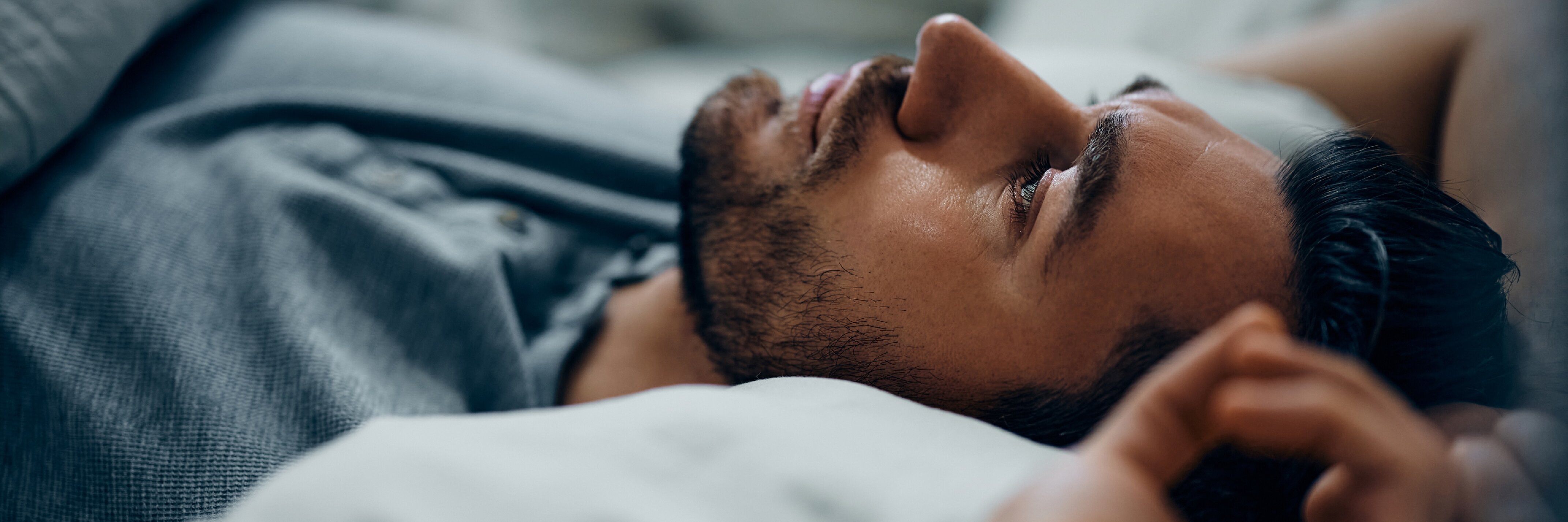 Ein Mann liegt auf dem Rücken im Bett und blickt nach oben.
