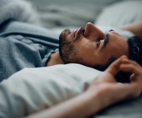 Ein Mann liegt auf dem Rücken im Bett und blickt nach oben.